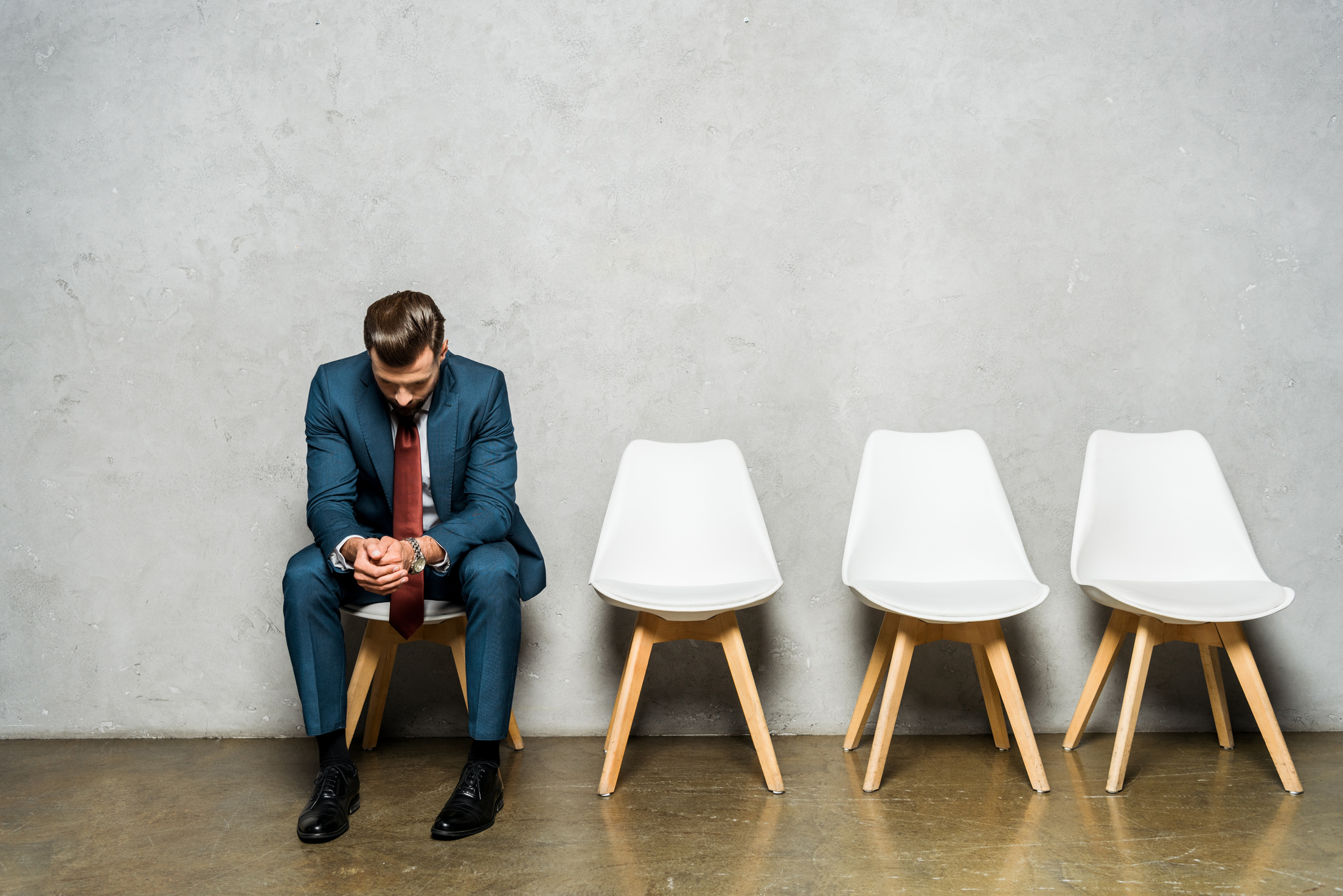 handsome man sitting with clenched hands on white chair while waiting job interviw